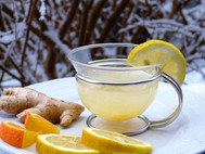Photo of a cup of hot lemon tea, with slices of lemon and orange, and whole ginger root