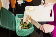 Food scraps being scraped with knife off cutting board into countertop organics container