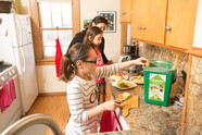 Girl in kitchen with family putting food scraps into organics recycling container