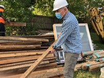 Man carrying piece of lumber being salvaged in deconstruction project