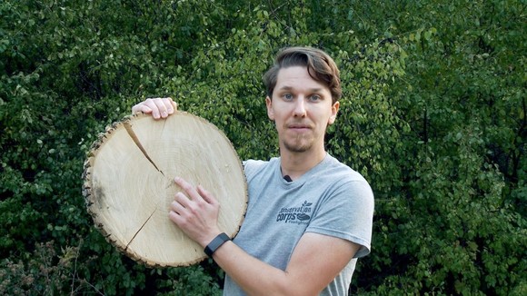 Educator holding up a slice of a tree trunk pointing out growth rings