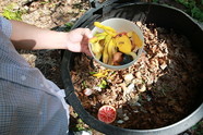 Hand holding bucket of food scraps being placed in compost bin