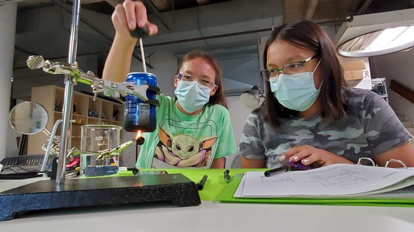 Students wear masks while conducting a science experiment and taking notes