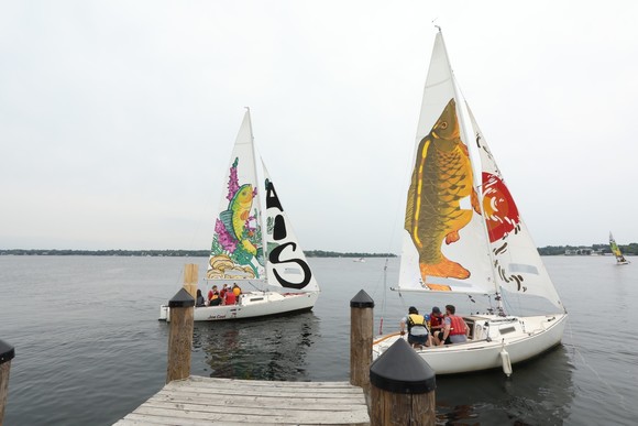 Sailboats with painted sails to raise awareness about aquatic invasive species leaving the dock