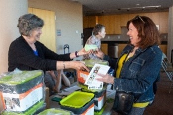 Woman picking up a compostable bag from another woman behind a table