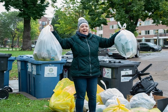 Triumphant woman in coat holding up bags of garbage collected at community clean up event