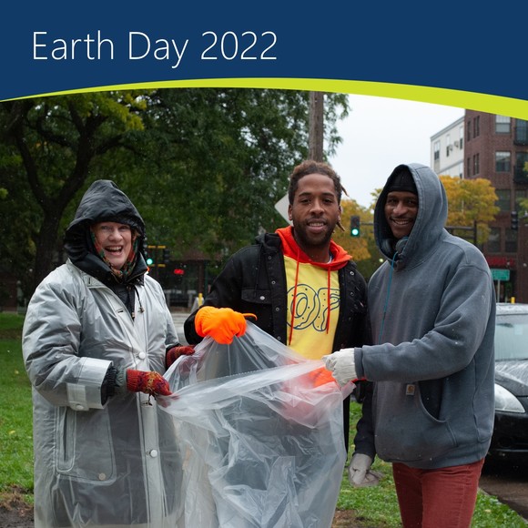 Three people wearing rain coats hold open trash bag during litter cleanup