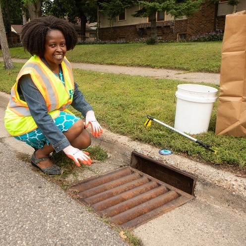 Woman in safety vest crouching next to an adopted storm drain