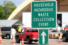 Household hazardous waste collection event sign with cars unloading in background