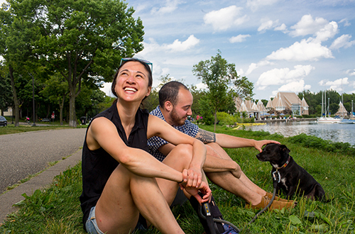 Two people sitting with dog on grass by lakeshore