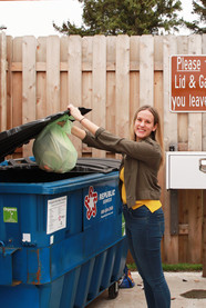 Woman putting organics bag into a drop-off dumpster