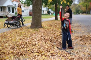 Young boy and parents raking leaves out of street