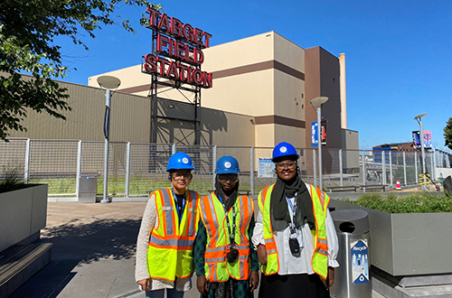 Three green pathways interns in hard hats and safety vests outside the Hennepin Energy Recovery Center by the Target Field sign
