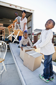 Family including parents and two kids unloading boxes and chairs from moving truck