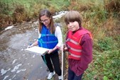 Child and adult stand by stream and conduct a survey
