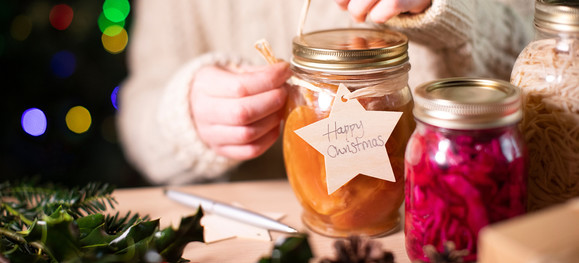 Person tying a "happy Christmas" tag onto a jar of canned peaches