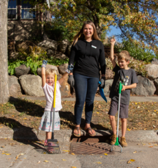 Mom and two kids holding tools celebrating in front of storm drain