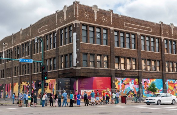 The Coliseum building with building gathered out front and murals around the ground floor.