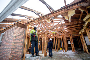 Two construction workers inside the framing of a house being deconstructed