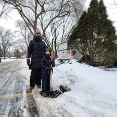 Mom and son bundled up with shovel standing over a cleared storm drain surrounded by snow and ice