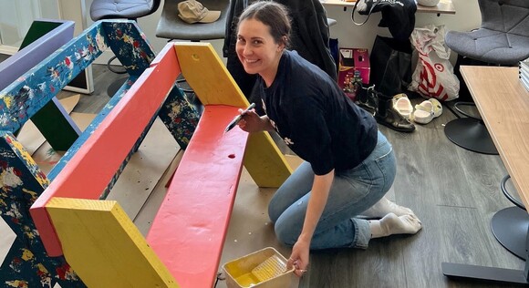 Person smiling while painting a bench