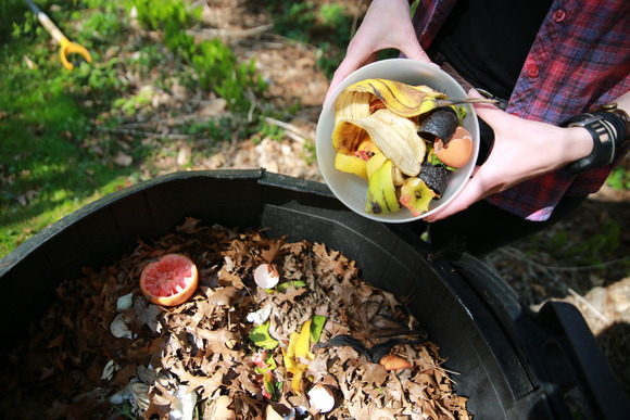 Closeup of someone holding a small bucket of food scraps over a compost pile