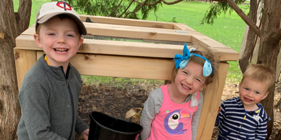 Three kids in front of a compost bin