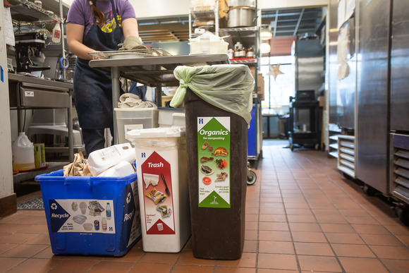 Recycling, trash, and organics recycling bins set up in a commercial kitchen