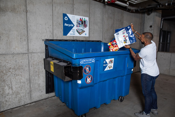 Man dumping recyclables from reusable tote into dumpster