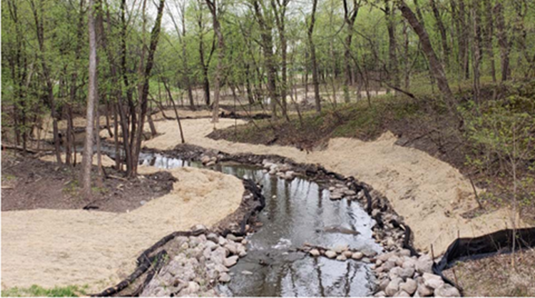 Creek meandering through forest with rock and straw on restored banks