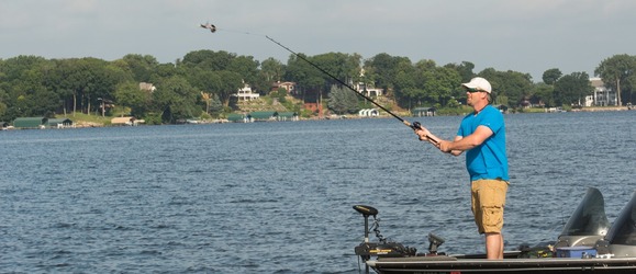 Man standing on a boat on a suburban lake casting a fishing lure