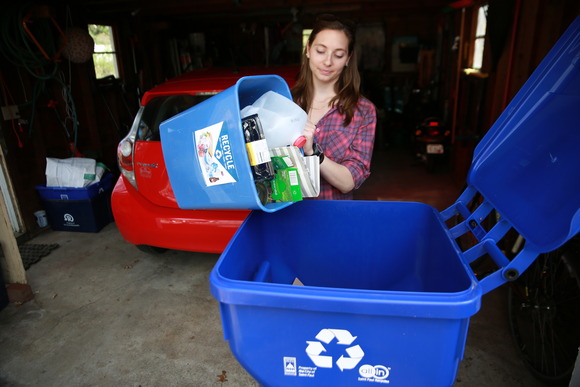 Woman dumping small bin of recyclables into recycling cart in a garage