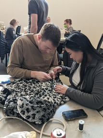 Woman working on mending some fabric with a Fix-It Clinic volunteer