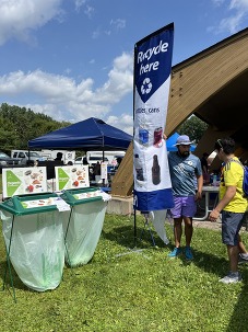 Hennepin County staff standing beside portable organics recycling containers and a recycle here banner outside a picnic shelter