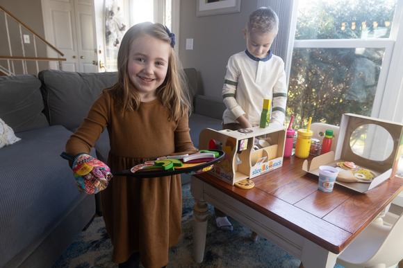 Young girl holding a try of toy food with young boy in background