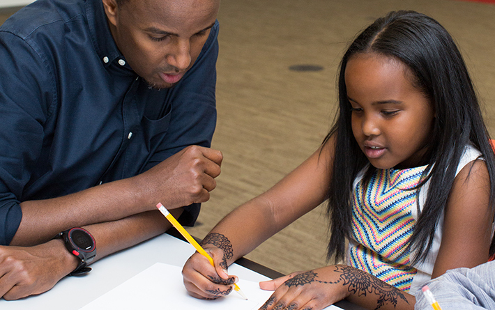 staff person looks at blank paper with child holding pencil