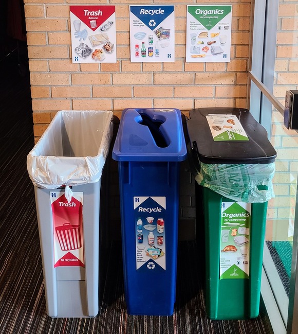 Set of recycling, organics, and trash bins against a brick wall at Hope of Prayer