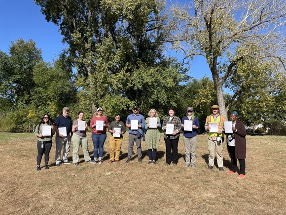 Group at environmental education network meeting standing in front of trees holding pictures they drew