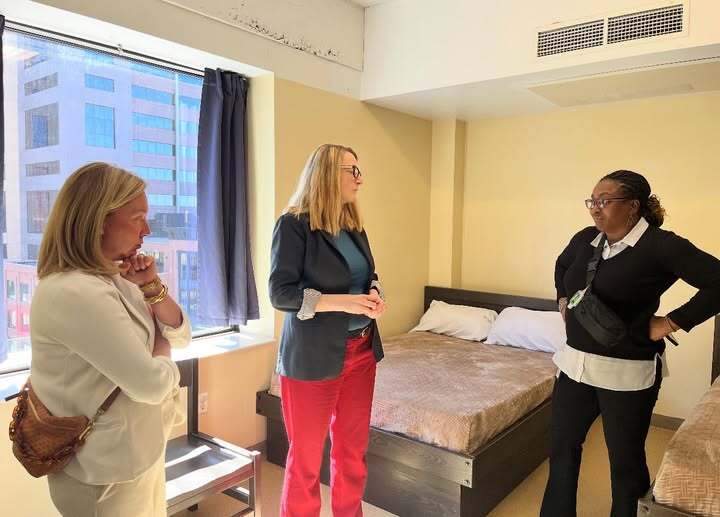 Heather and Commissioner Marion Greene stand in a room at the People Serving People shelter while listening to a staff member.