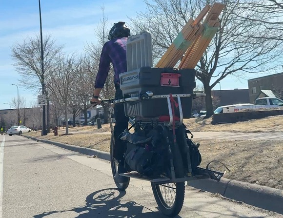 person riding a bike with lumber in an attached tote