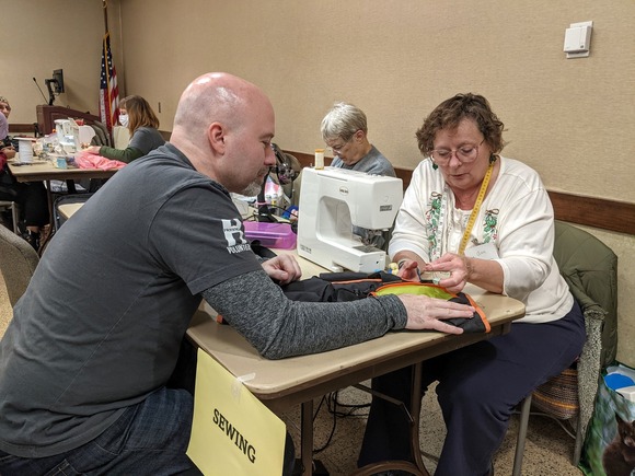 Fix-It Clinic volunteer and resident at a sewing machine working on mending clothing items