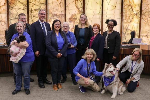 Heather smiles and pets  a dog in front of the dais after a County Board meeting. 