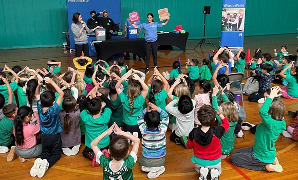students making hand signals about recycling at an assembly in a gym