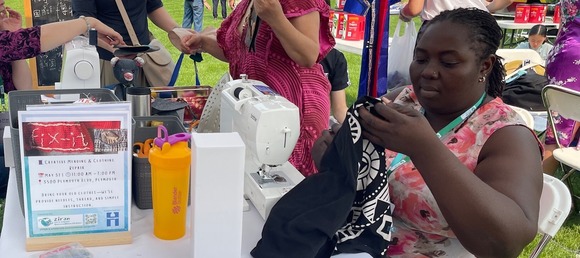 Person at an outdoor event with a sewing machine repairing a piece of clothing