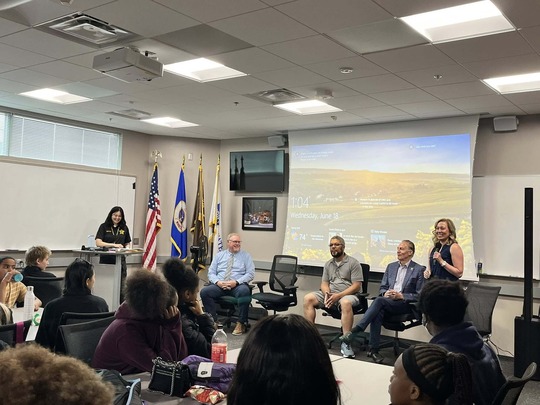 Heather speaks into a microphone alongside panelists at the Hennepin County Sheriff's Office Youth Leadership Academy.