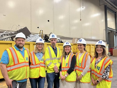 Heather poses with staff at the Brooklyn Park Recycling Center; they are wearing protective gear and smiling.