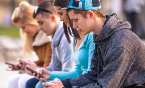 Stock photo showing teenagers sitting down and looking at their phones.