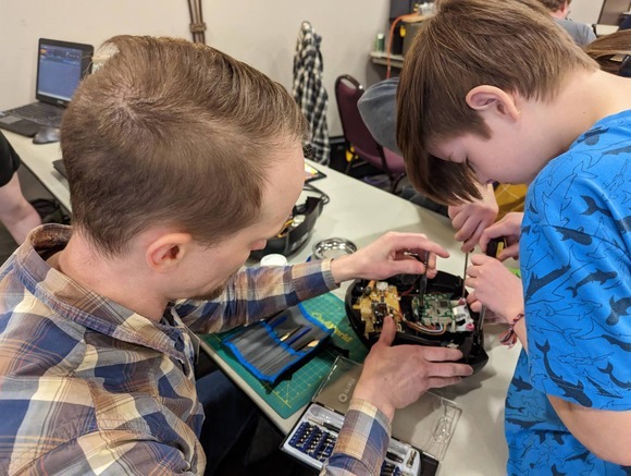 Event volunteer fixing a broken electronic with a boy