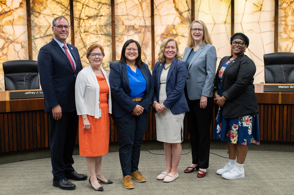 Commissioners stand in the Board room: Kevin Anderson, Debbie Goettel, Irene Fernando, Heather Edelson, Marion Greene, and Angela Conley.