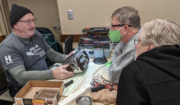 Three people working together to fix electronics
